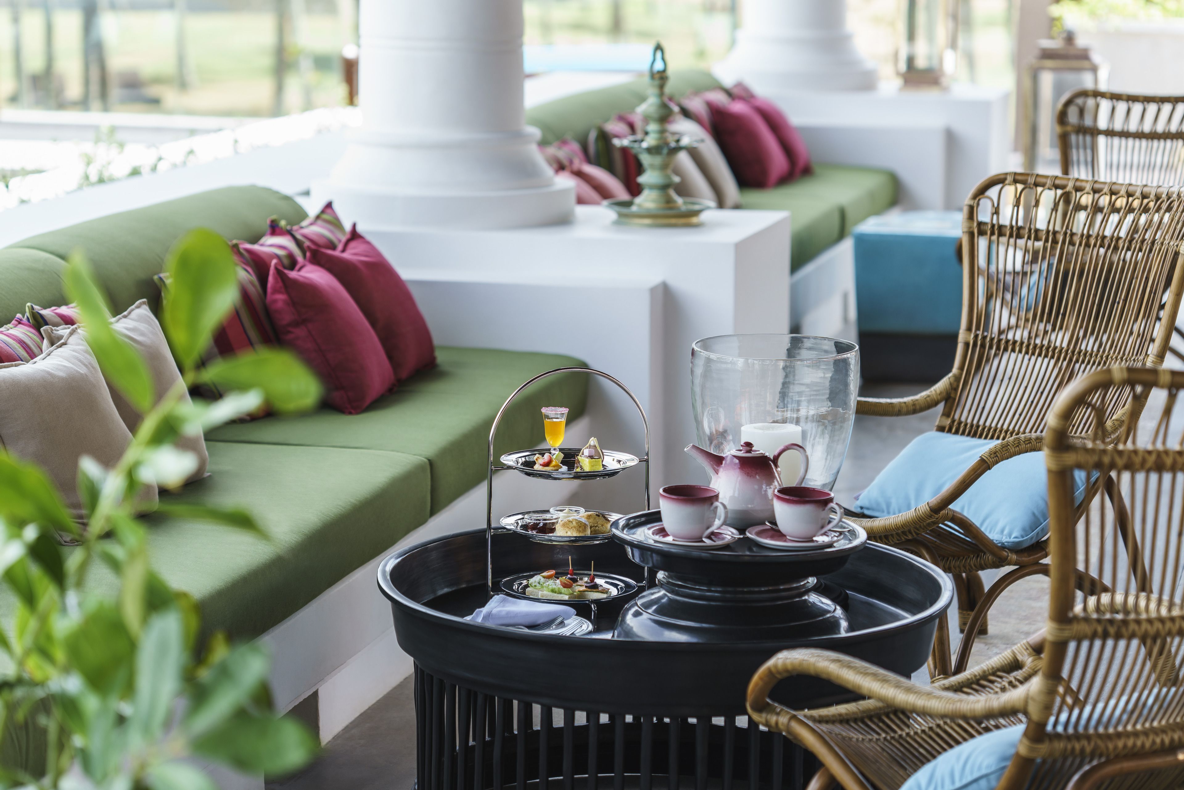 A cozy seating area with a green sofa, wicker chairs, and a table set with tea service and snacks.