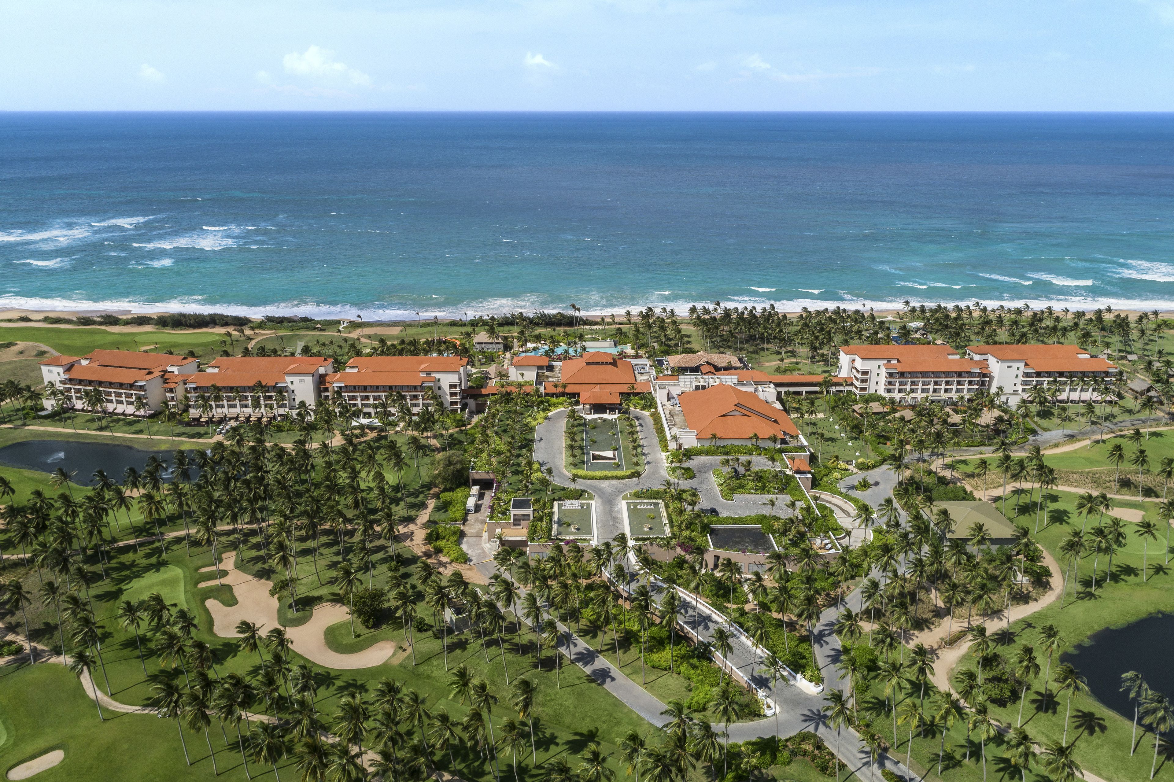 A resort with multiple buildings, a golf course, and a beach view.