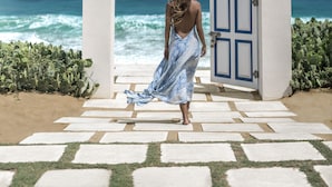 Una mujer con un vestido azul camina hacia una puerta con vista al océano.
