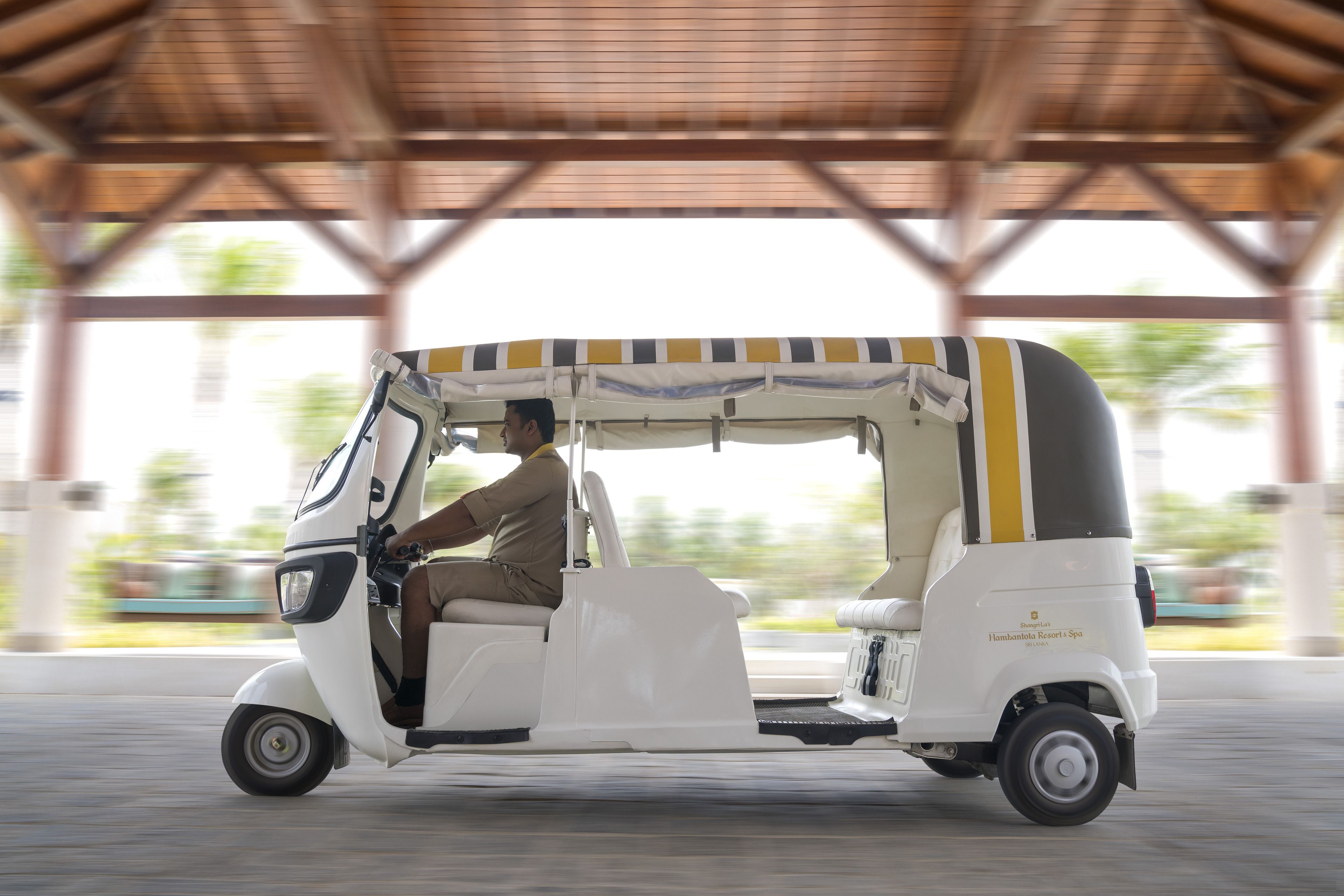 A white auto-rickshaw parked under a covered area with a roof structure.