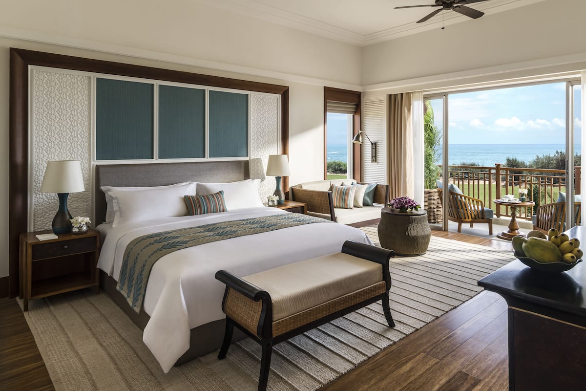 Een ruime slaapkamer met een groot bed, een zithoek met uitzicht op de oceaan en een balkon met een tafel en stoelen.
