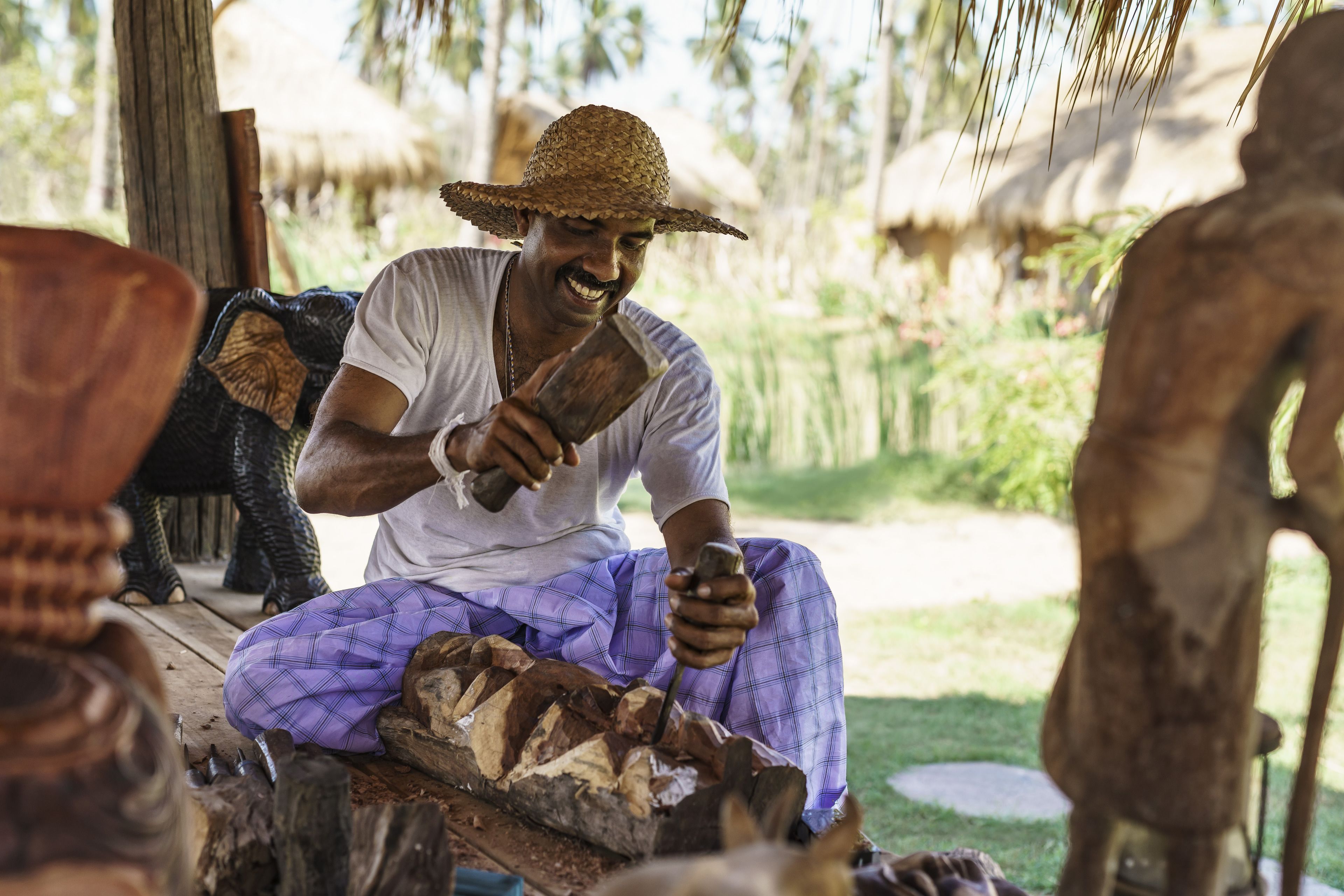 A person sitting outdoors, working with wooden objects.