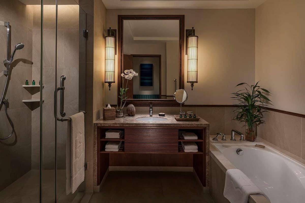 Een moderne badkamer met een douchecabine van glas, een vrijstaand bad en een wastafel met een grote spiegel en wandlampen.