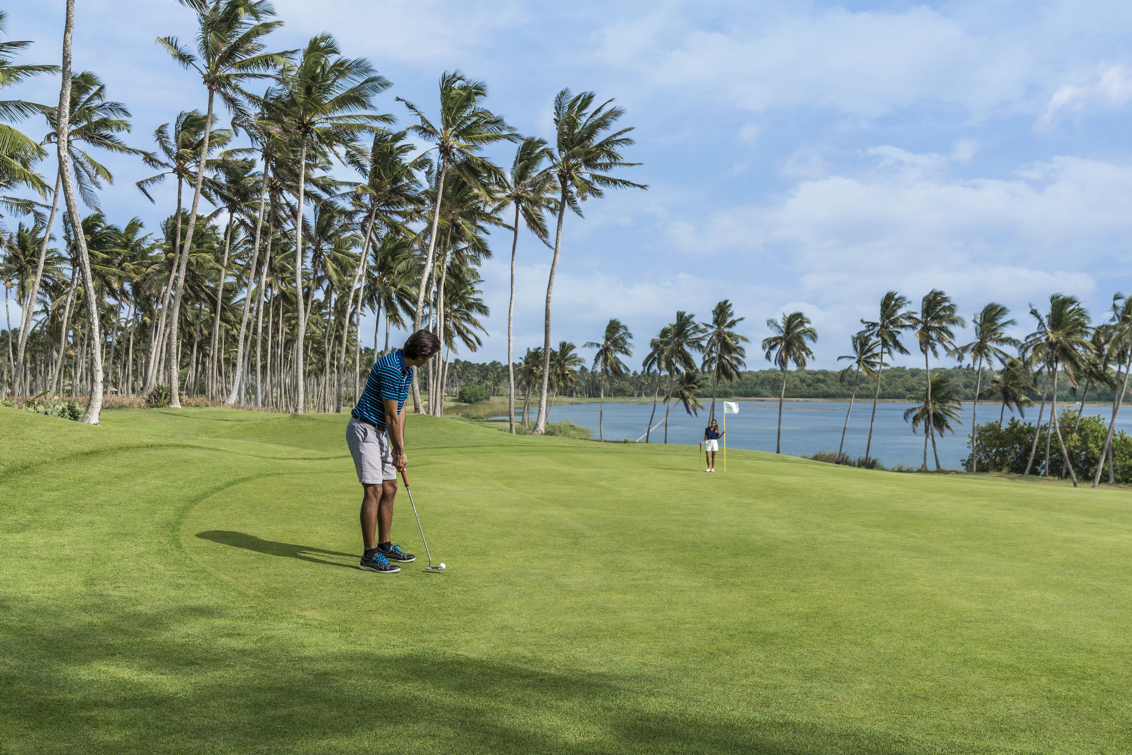 A golf course with a water body and palm trees in the background.