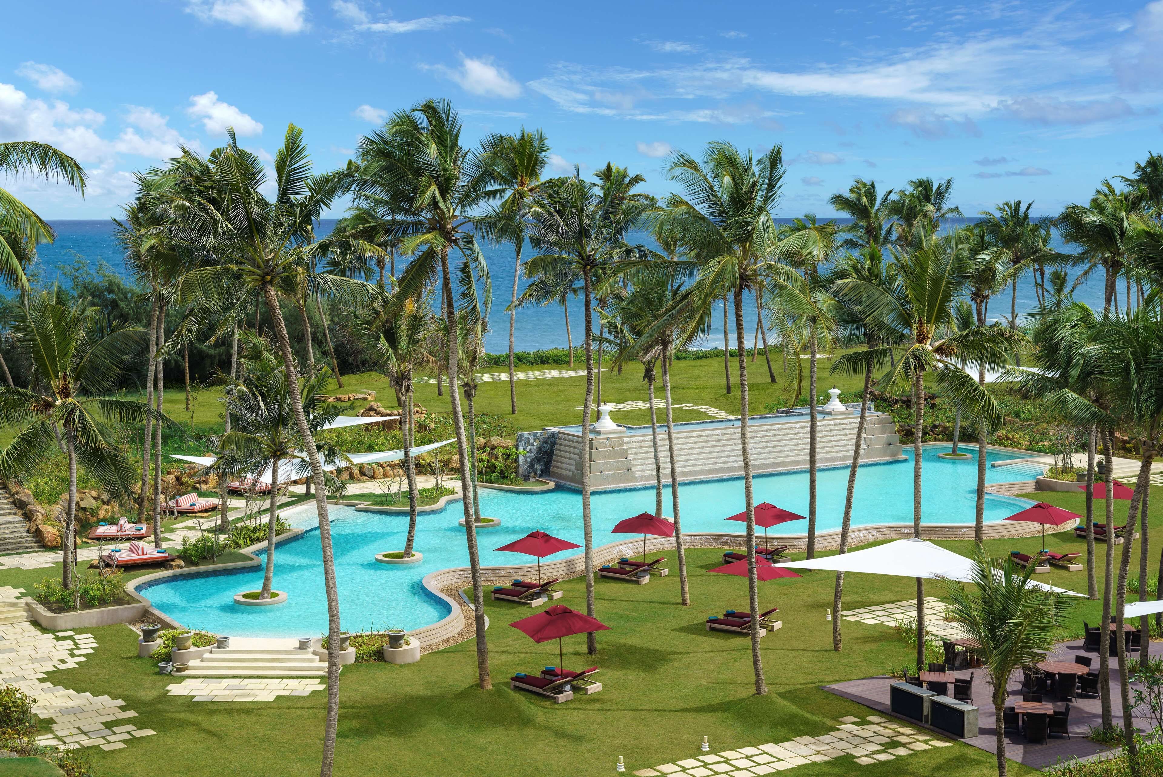 Un resort con piscina rodeada de palmeras, sillas de descanso y sombrillas.