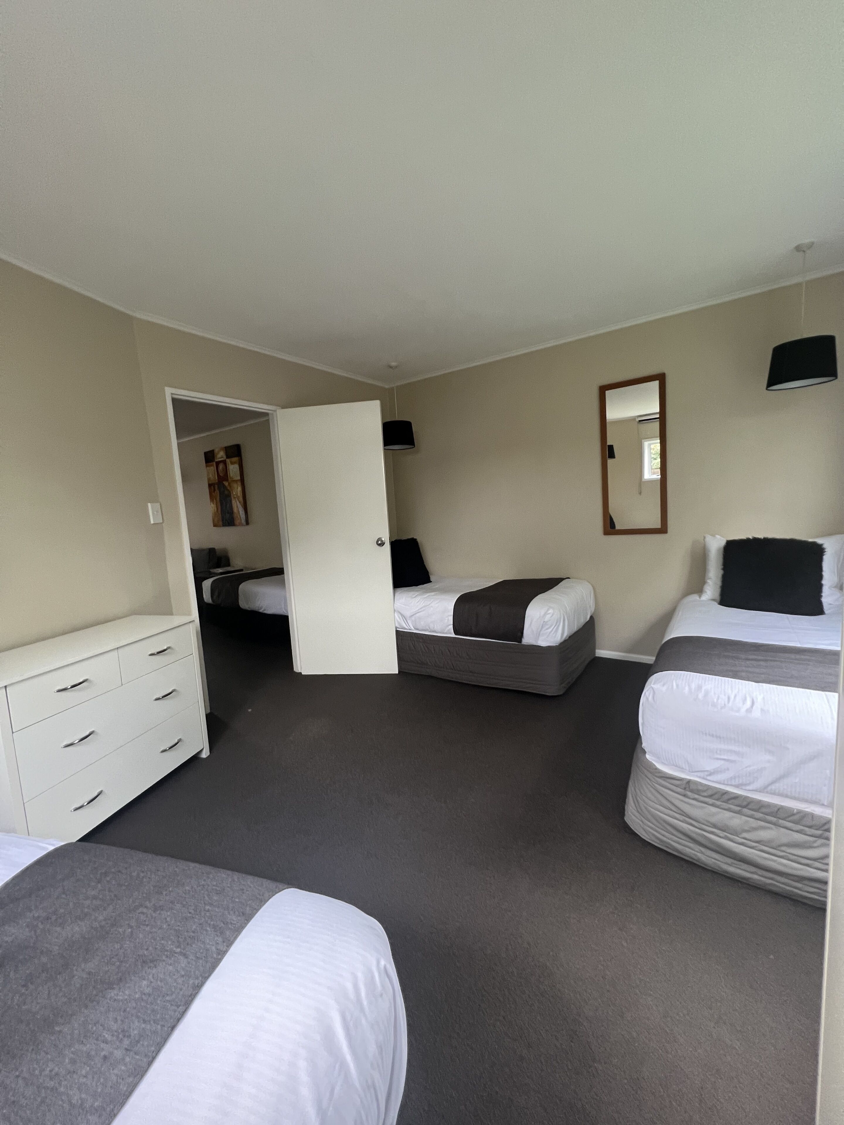 A hotel room with two beds, a dresser, a mirror, and a door leading to another room.