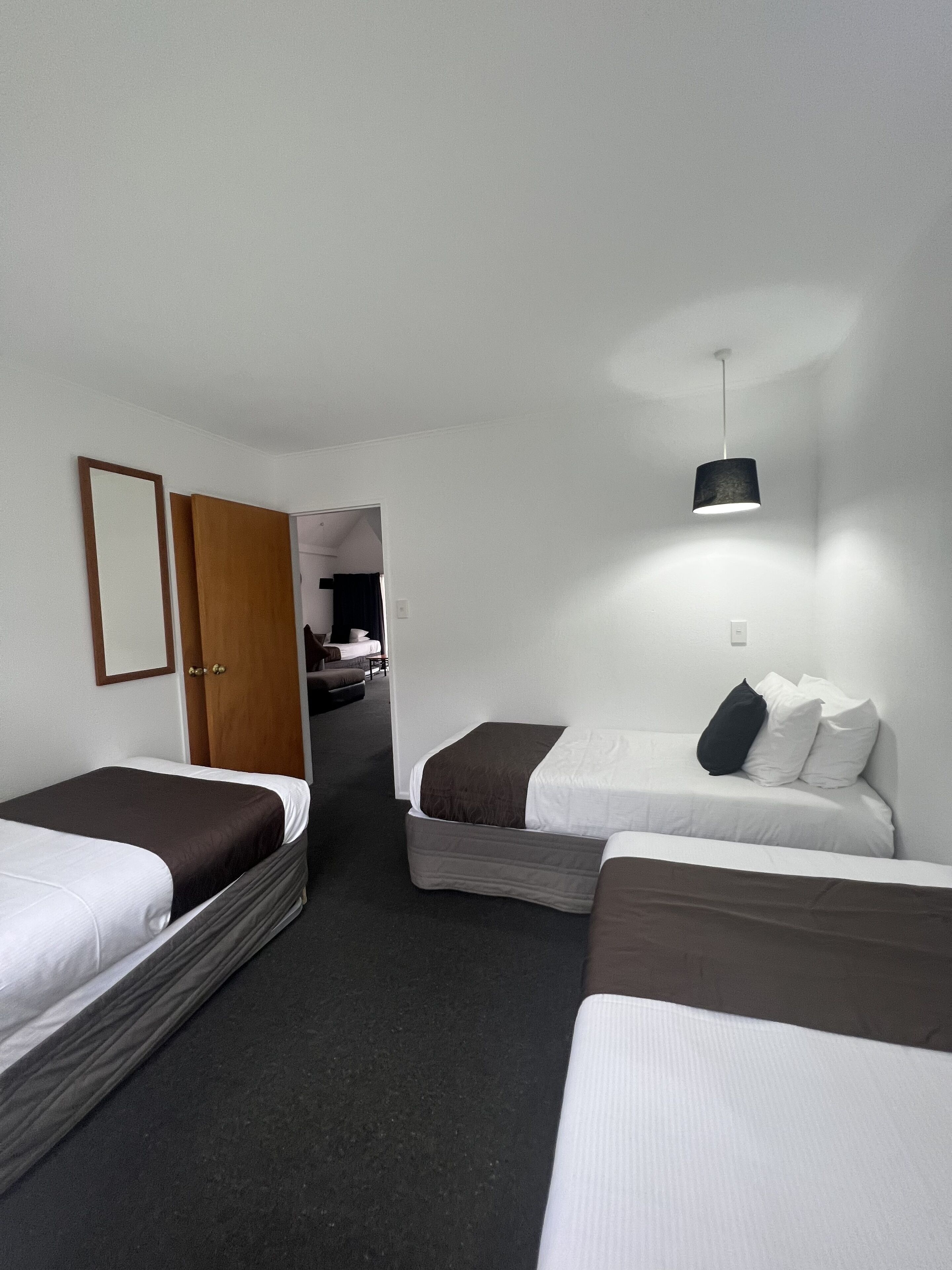 A hotel room with two single beds, a wooden door, a small table, and a hanging light fixture.