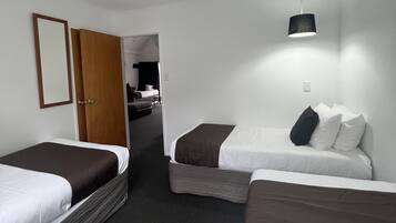 A hotel room with two single beds, a wooden door, a small table, and a hanging light fixture.