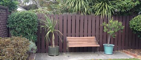 A wooden bench in a garden with a wooden fence, potted plants, and a well-maintained lawn.