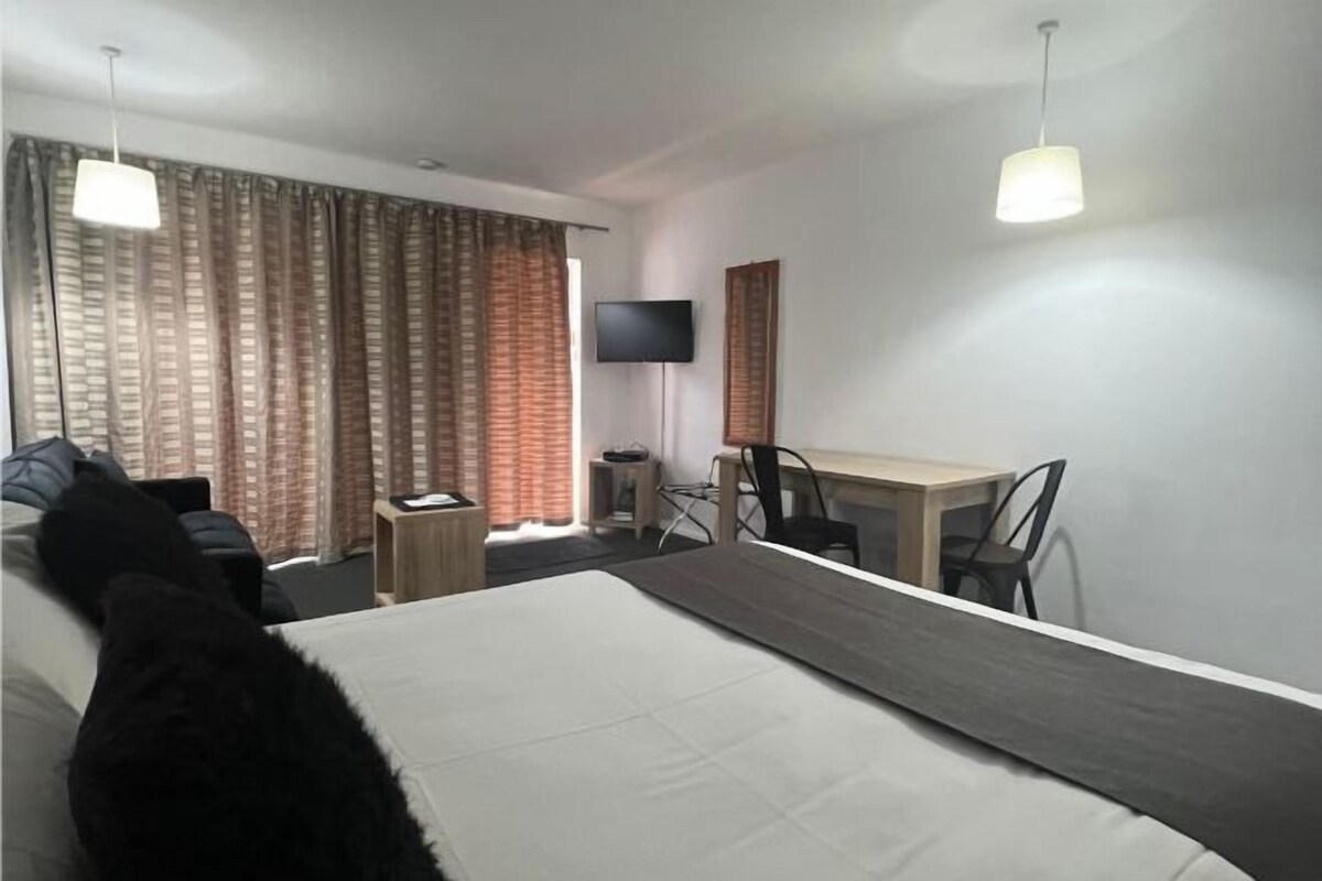 Ein Hotelzimmer mit Bett, Schreibtisch, Stuhl, Fernseher und Vorhängen.