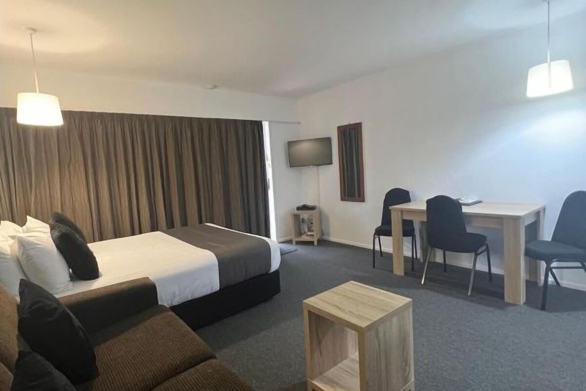 Ein Hotelzimmer mit einem Bett, einem Schreibtisch, einem Stuhl, einem Fernseher und einem kleinen Tisch.