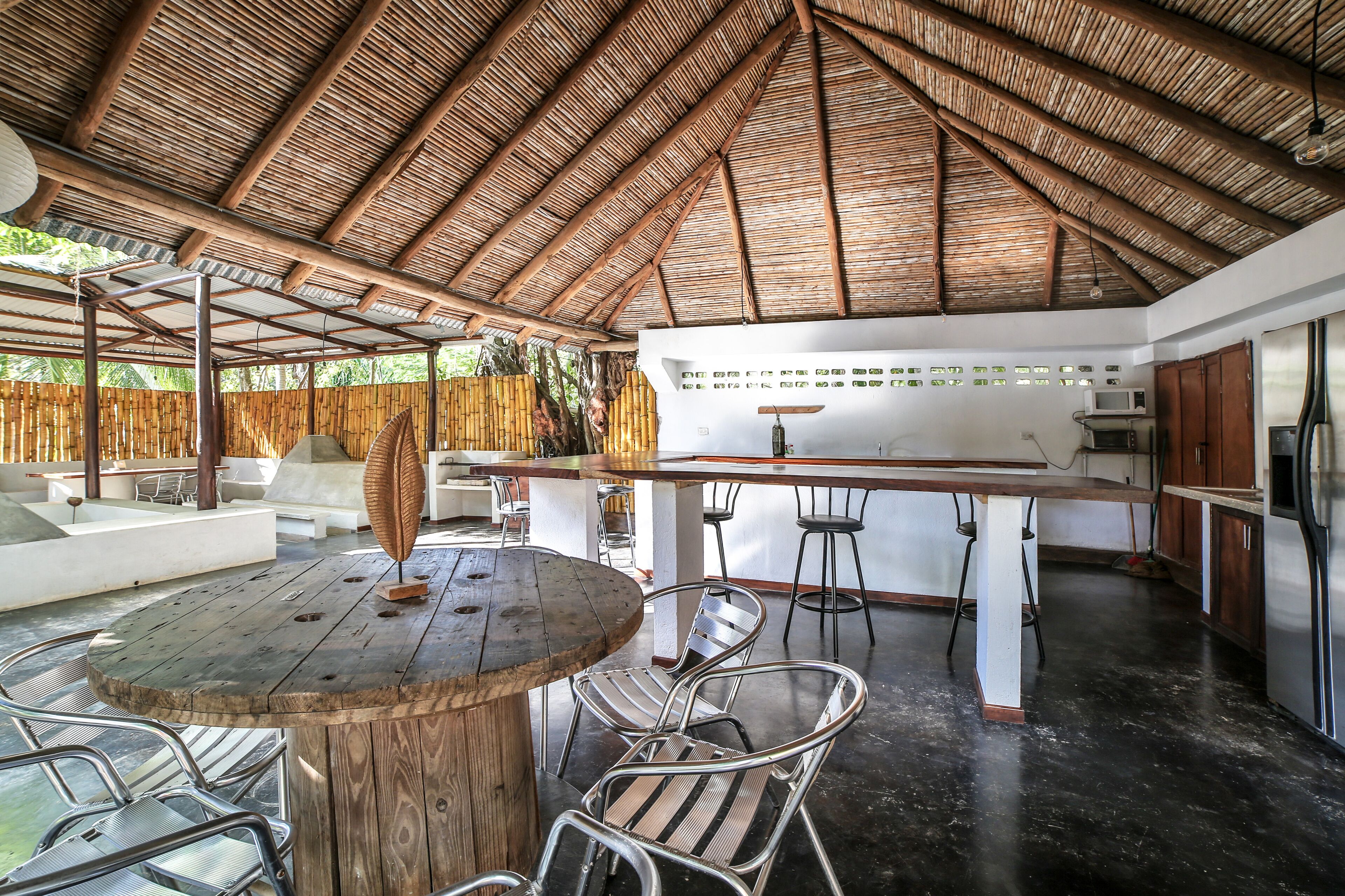 Un espacio exterior con comedor de mesa y sillas de madera, una zona de bar con taburetes y una cocina con electrodomésticos.