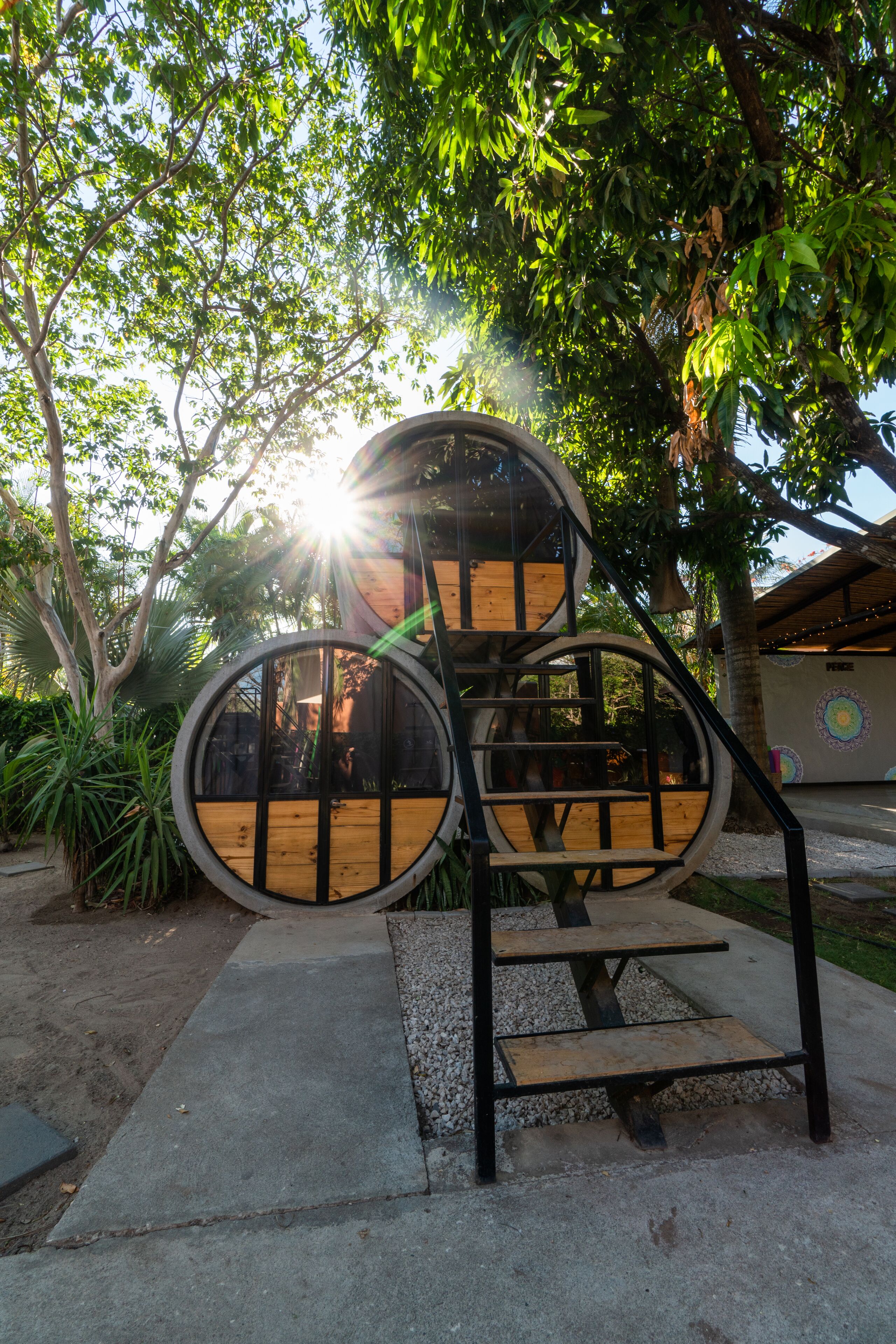 A circular wooden structure with a metal staircase, surrounded by trees and a concrete pathway.