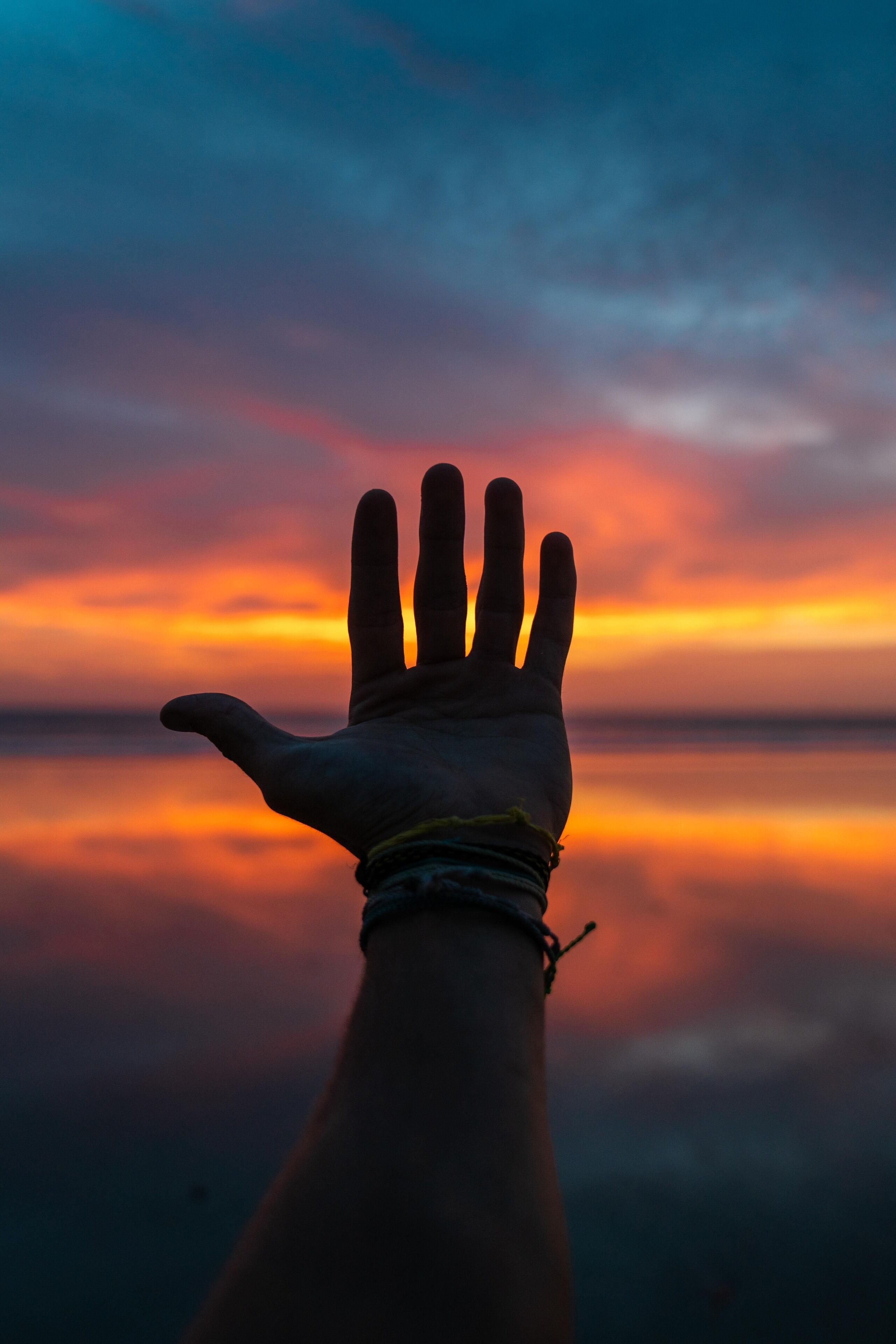 Una mano extendida contra un atardecer, con un mar tranquilo al fondo.