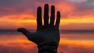 Una mano extendida contra un atardecer, con un mar tranquilo al fondo.