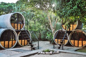 A structure made of large cylindrical wooden barrels arranged in a circular pattern, with a central staircase connecting them. - Pipe House Playa Grande (Cabo Velas)