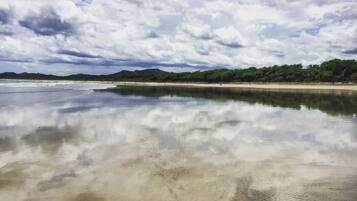 Una playa con aguas tranquilas que reflejan el cielo y colinas lejanas.