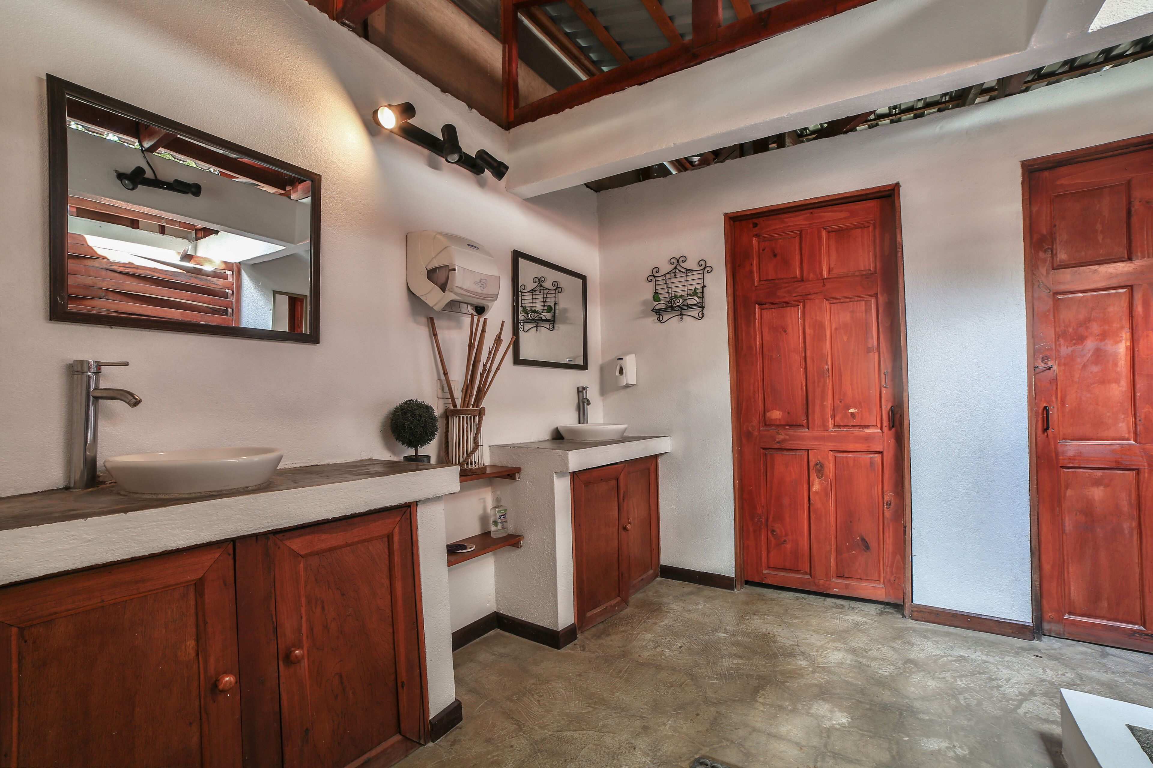 A bathroom with wooden cabinets, a white sink, and a large mirror. There are two wooden doors and a white wall with decorative wall art.