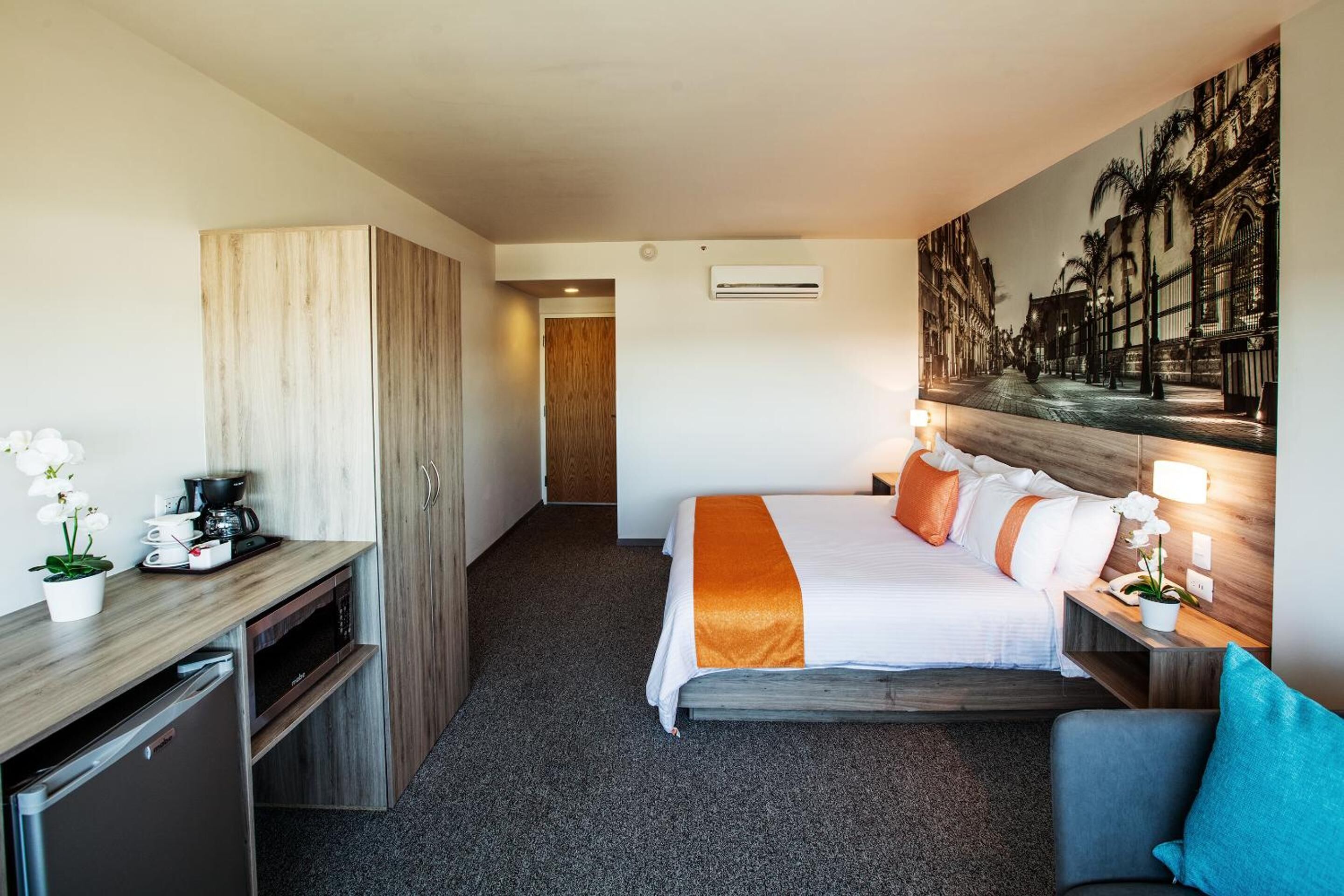 A hotel room with a bed, a desk, a wardrobe, and a hallway leading to another room.