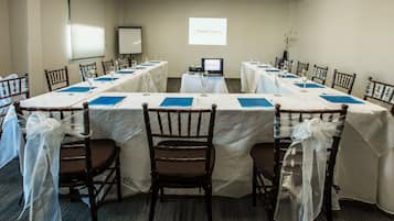 Un salón de conferencias con mesas largas, sillas y una pantalla de proyección que muestra 'Mission Express'.