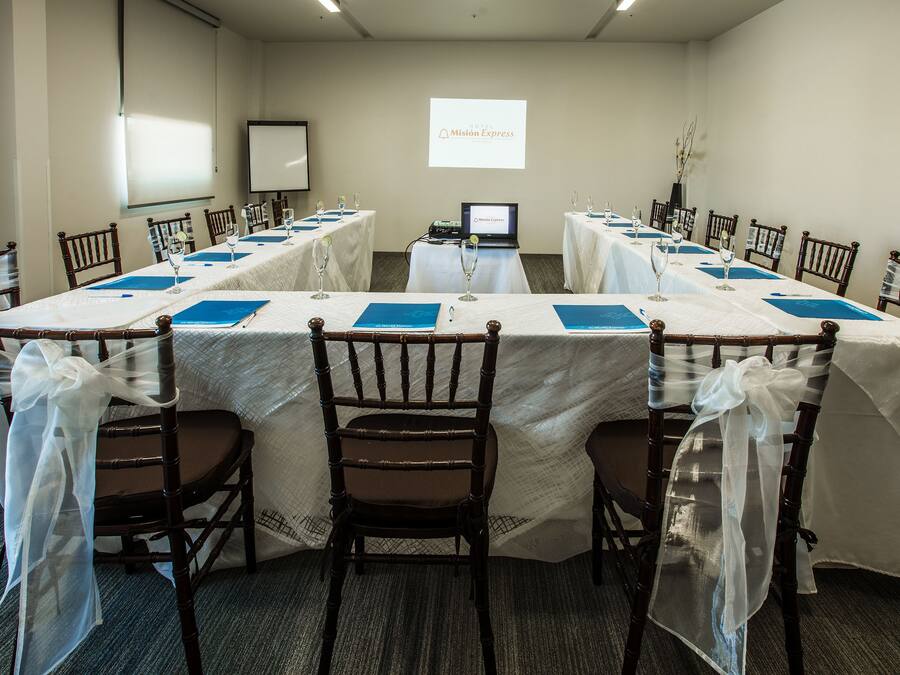 Un salón de conferencias con mesas largas, sillas y una pantalla de proyección que muestra 'Mission Express'.