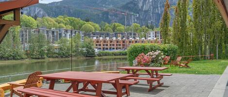 An outdoor patio with picnic tables and chairs, a river, and a mountainous backdrop.