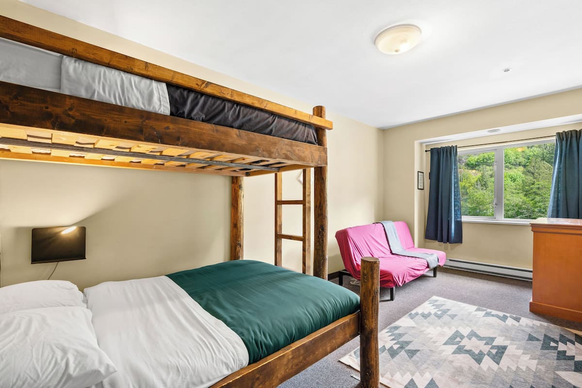 A bunk bed with a ladder, a desk, a chair, and a window with curtains.