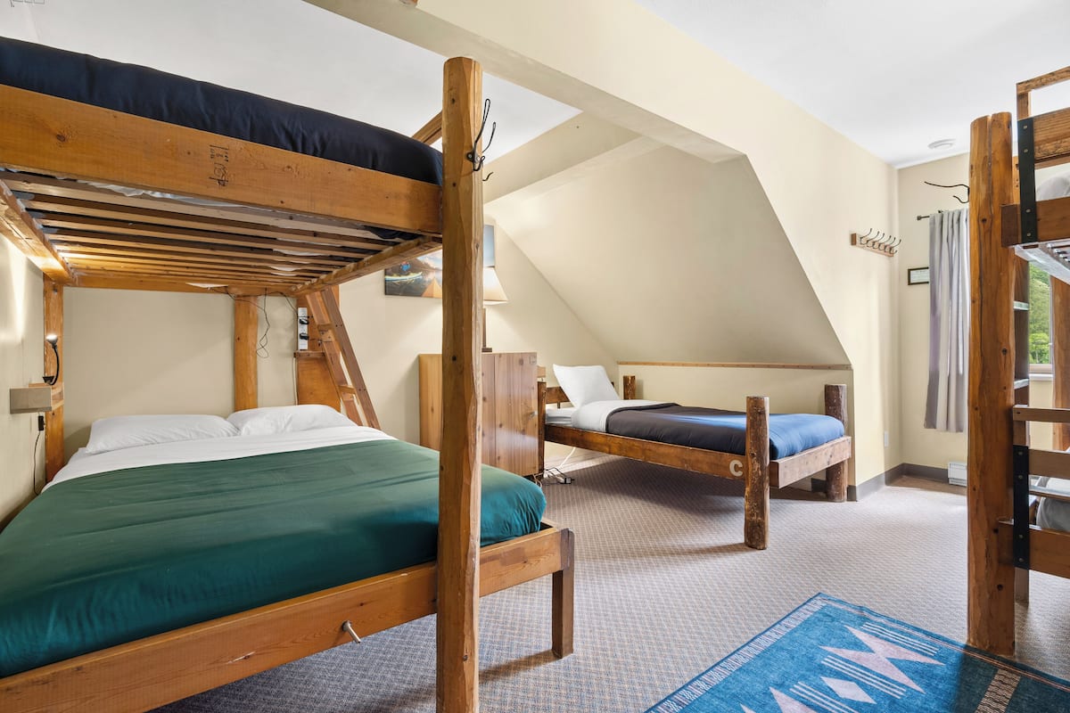 A dormitory-style room with bunk beds, a wooden ladder, and a blue patterned rug.