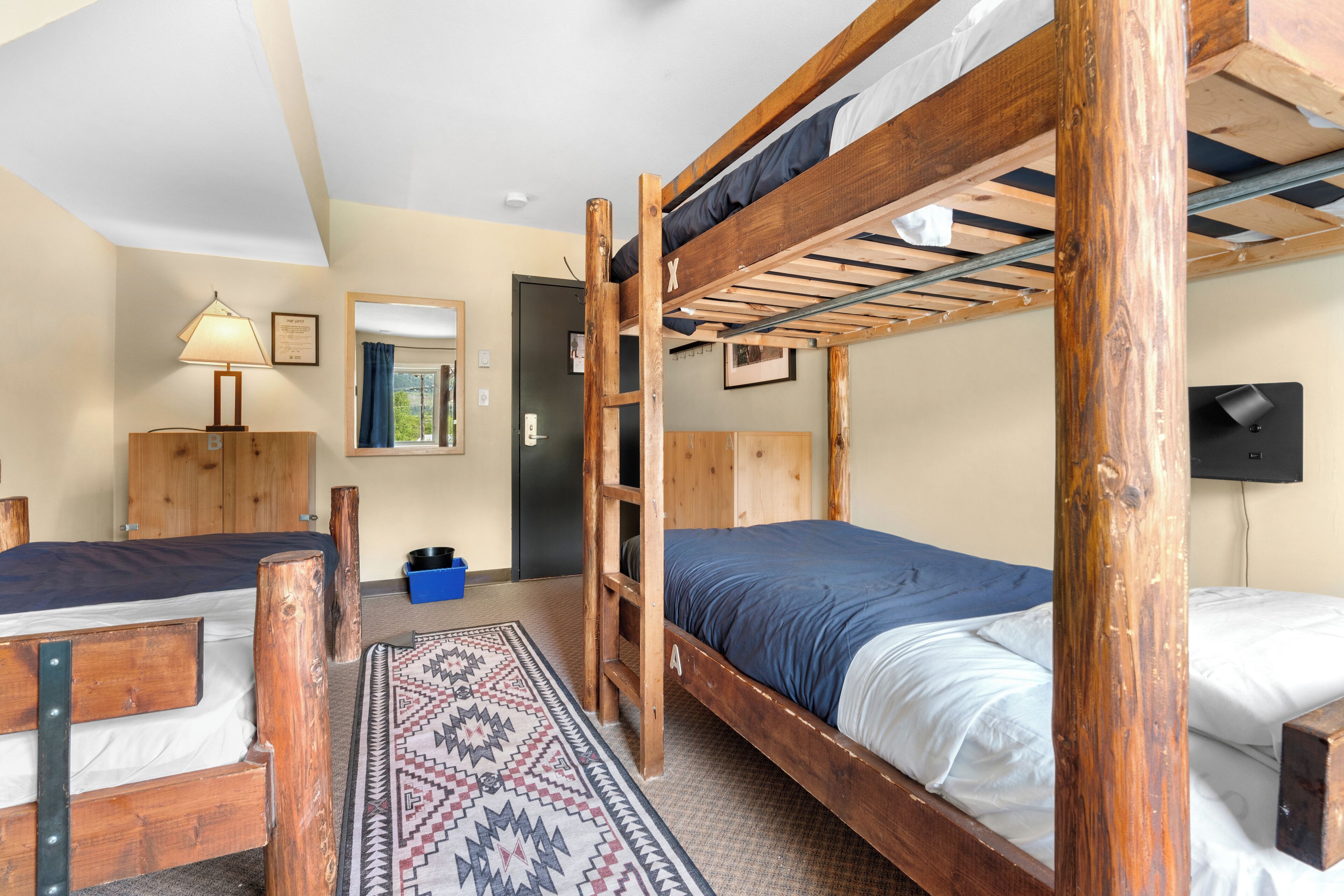 A room with two bunk beds, a wooden desk, a lamp, a mirror, and a patterned rug.