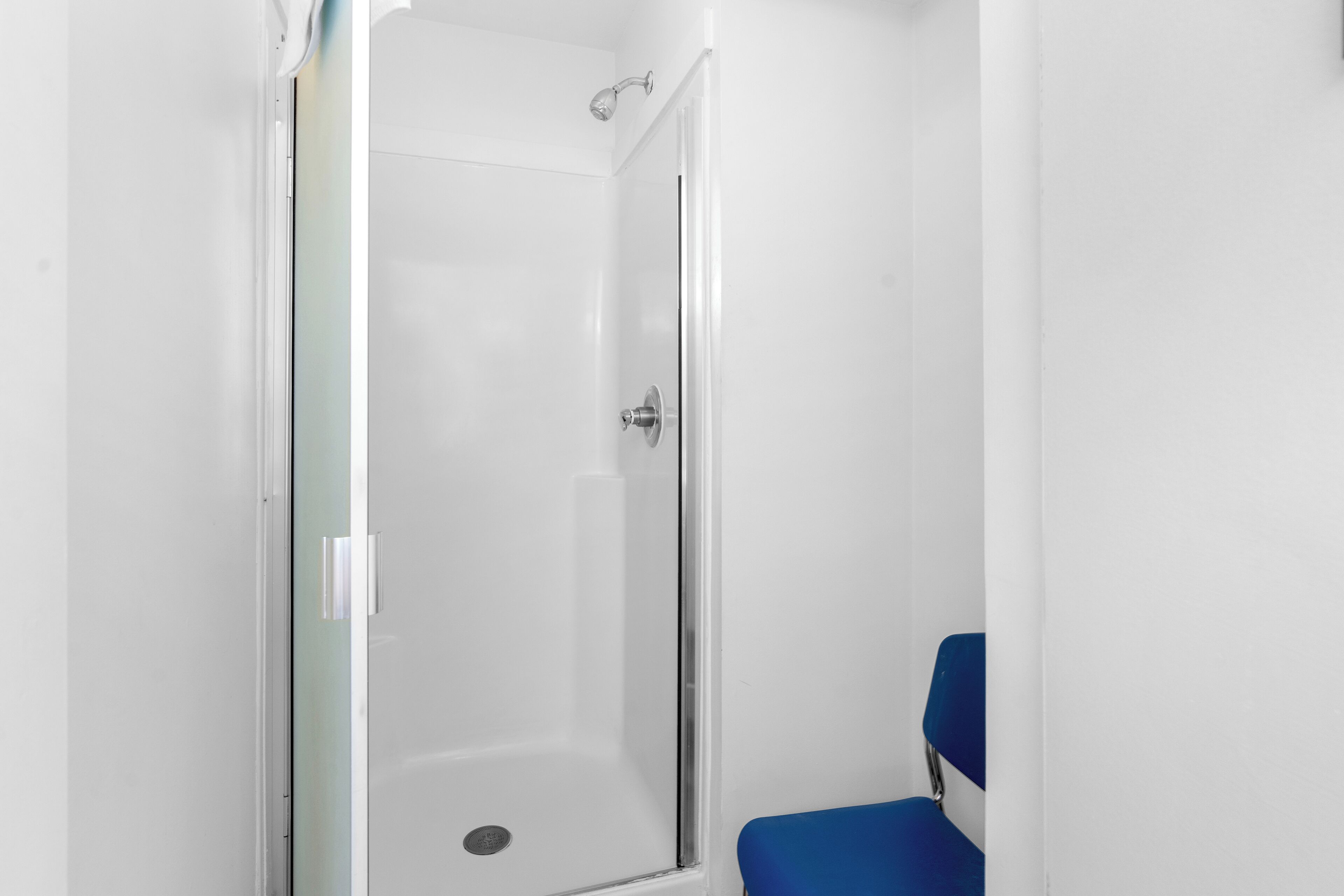 A small, enclosed shower area with a glass door and a blue chair.