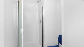 A small, enclosed shower area with a glass door and a blue chair.