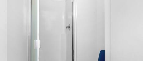 Un petit espace douche fermé, doté d’une porte en verre et d’une chaise bleue.