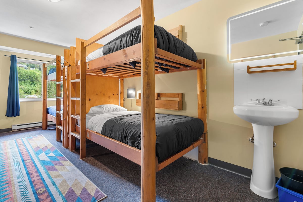 A bunk bed room with a wooden frame, a white sink, and a patterned rug.