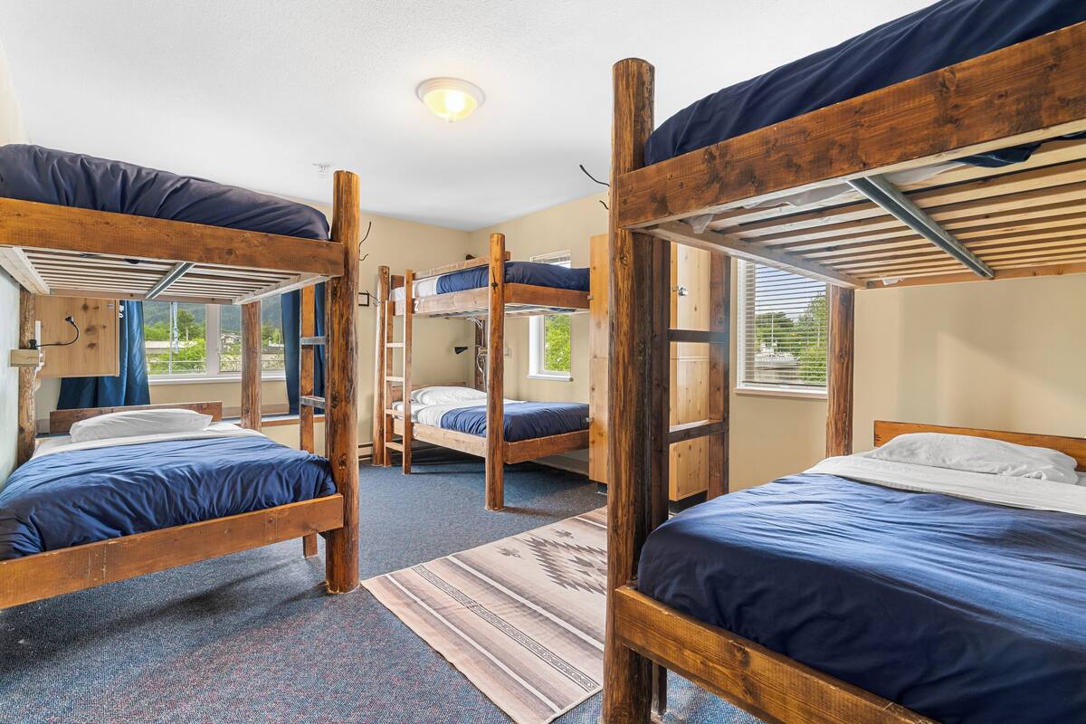 A dormitory room with bunk beds, a window, and a carpeted floor.