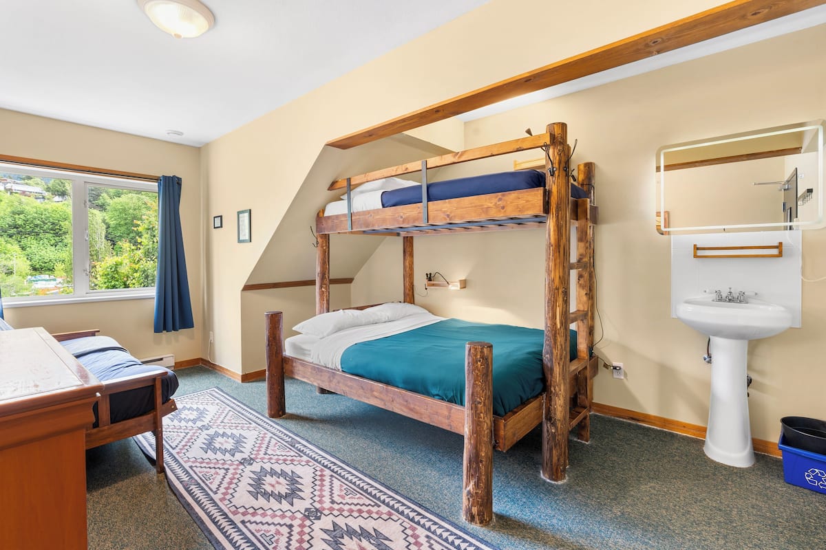 A bunk bed room with a window, a sink, and a patterned rug.