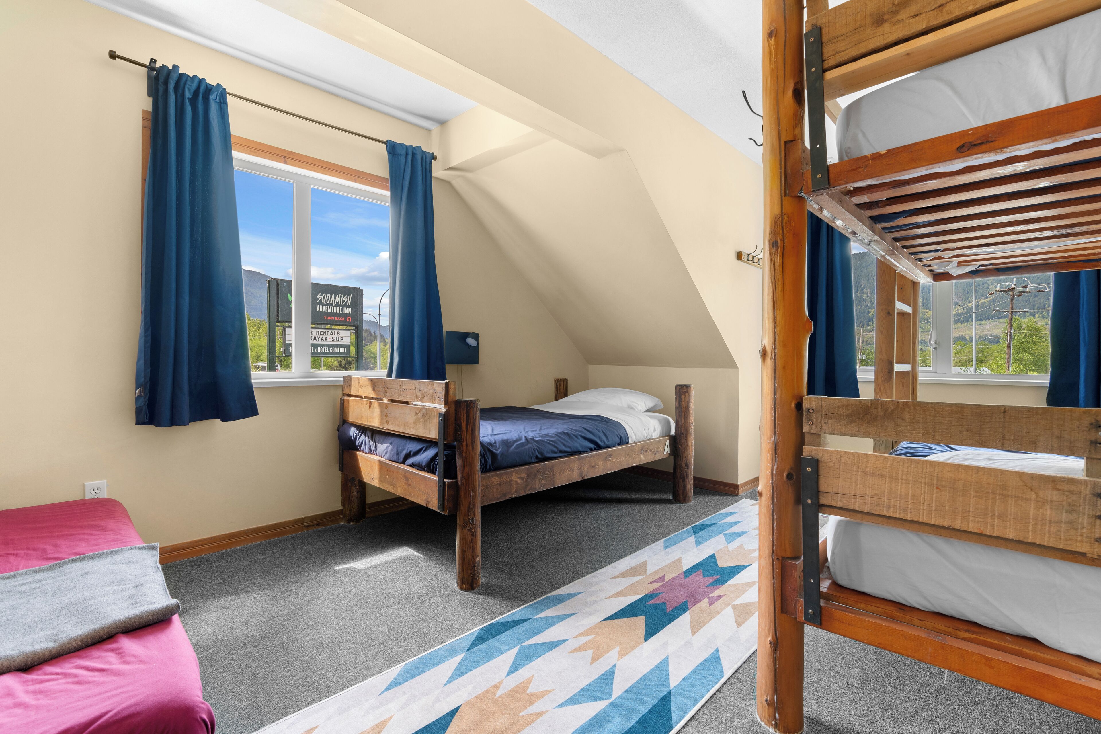 Une chambre de dortoir avec des lits superposés, une fenêtre avec des rideaux, un lit avec un oreiller et un tapis.