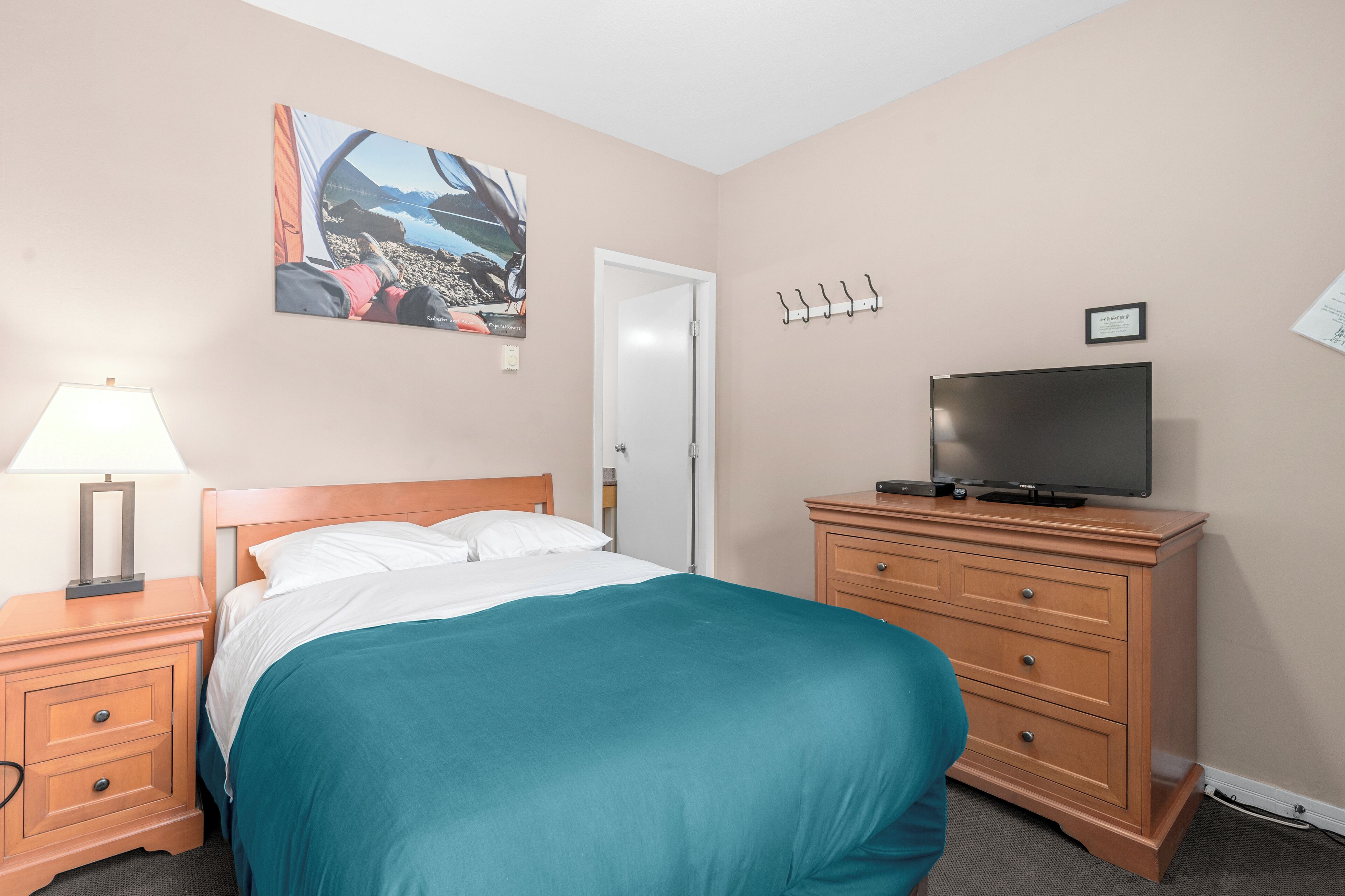 Une chambre d’hôtel avec un lit, un téléviseur posé sur une commode, une lampe et un tableau accroché au mur.