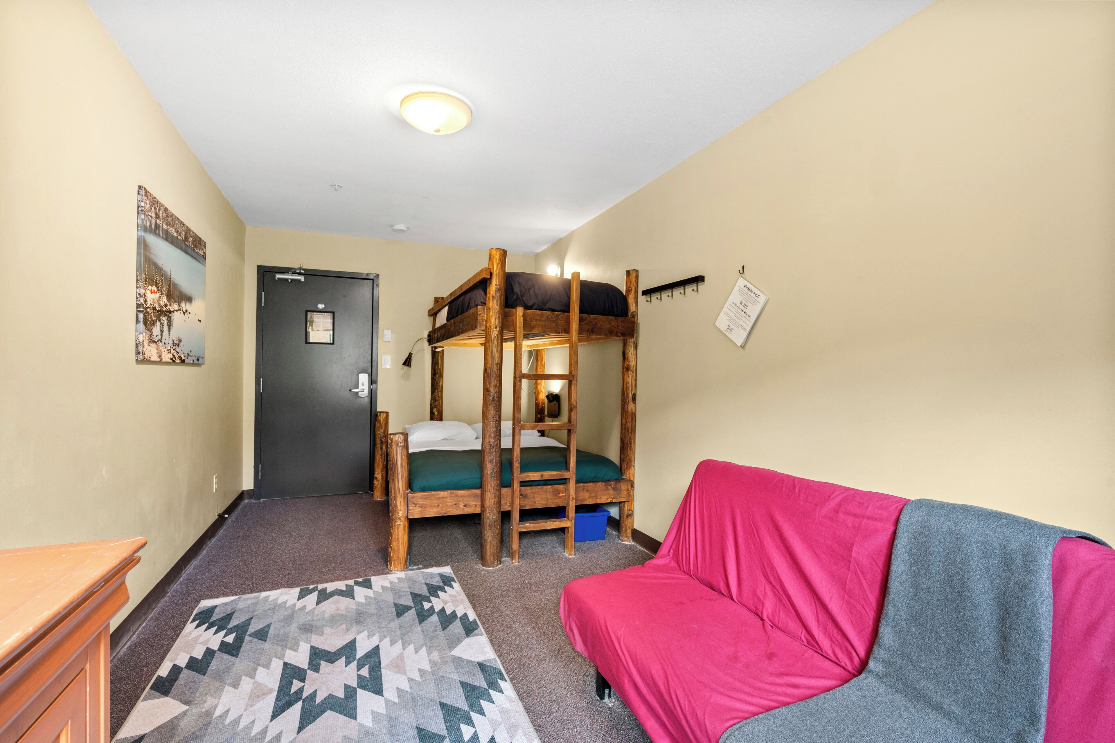 A dormitory room with bunk beds, a desk, a couch, and a patterned rug.