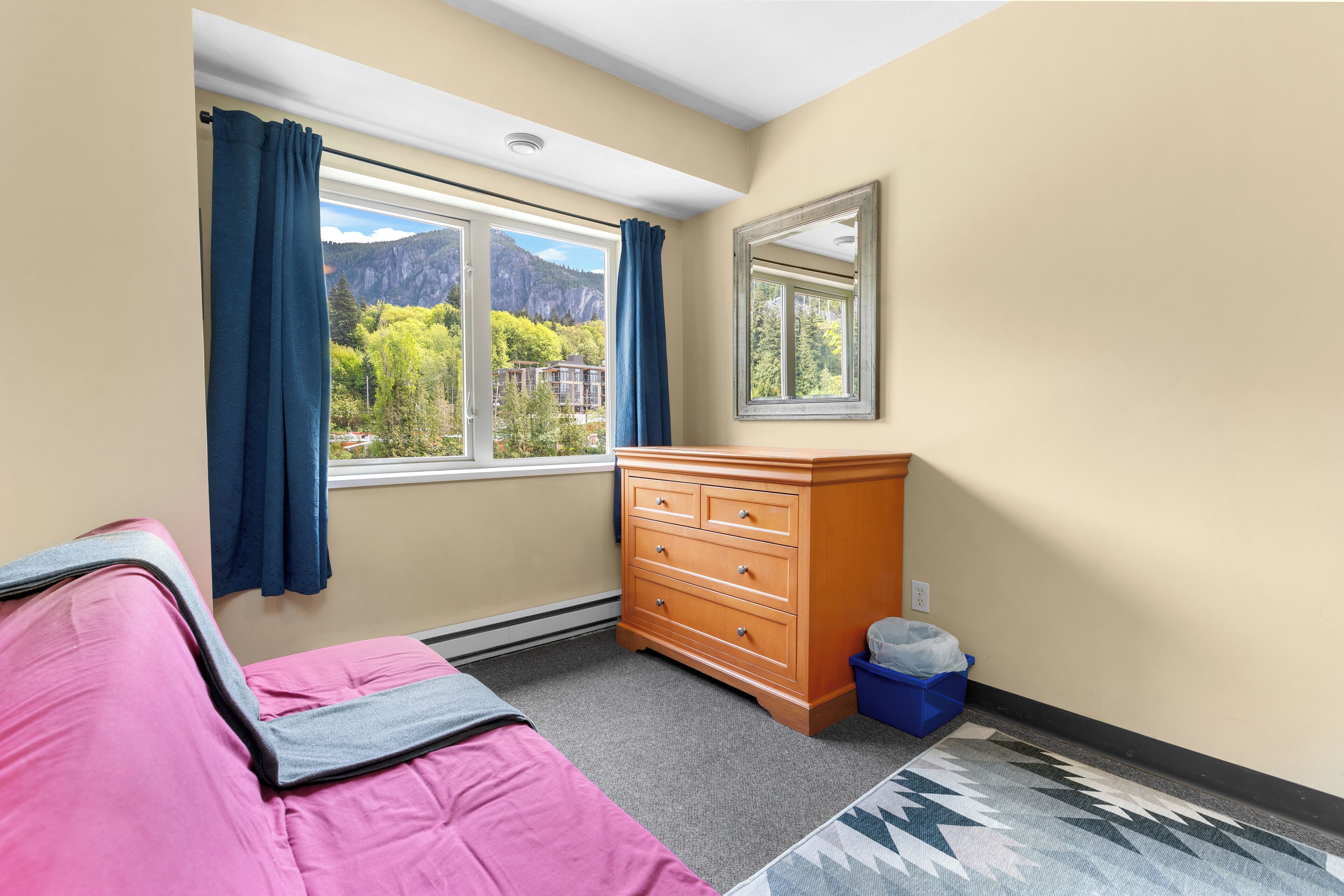 Quarto com cama, cômoda, janela com cortinas, espelho e vista para montanhas.