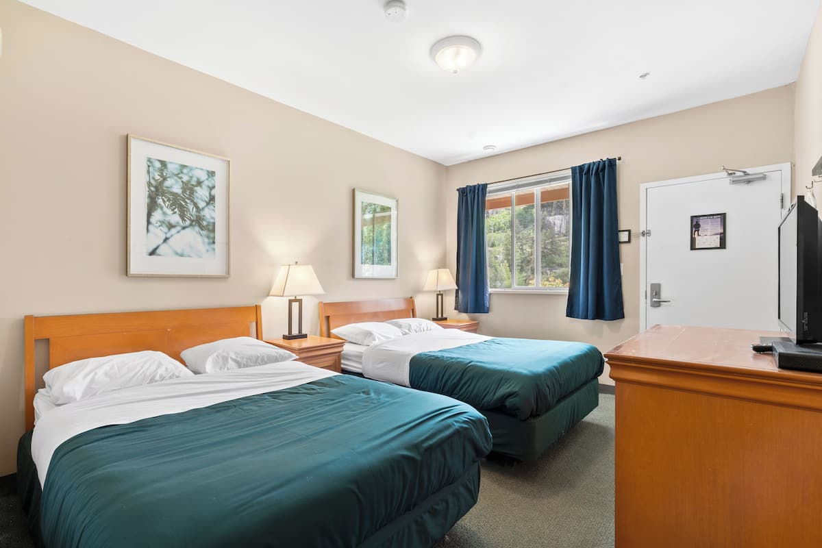 A hotel room with two single beds, a desk with a television, and a window with curtains.