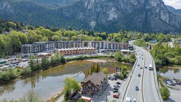 Un hotel moderno con varios pisos, estacionamiento y vistas a un río y montañas.