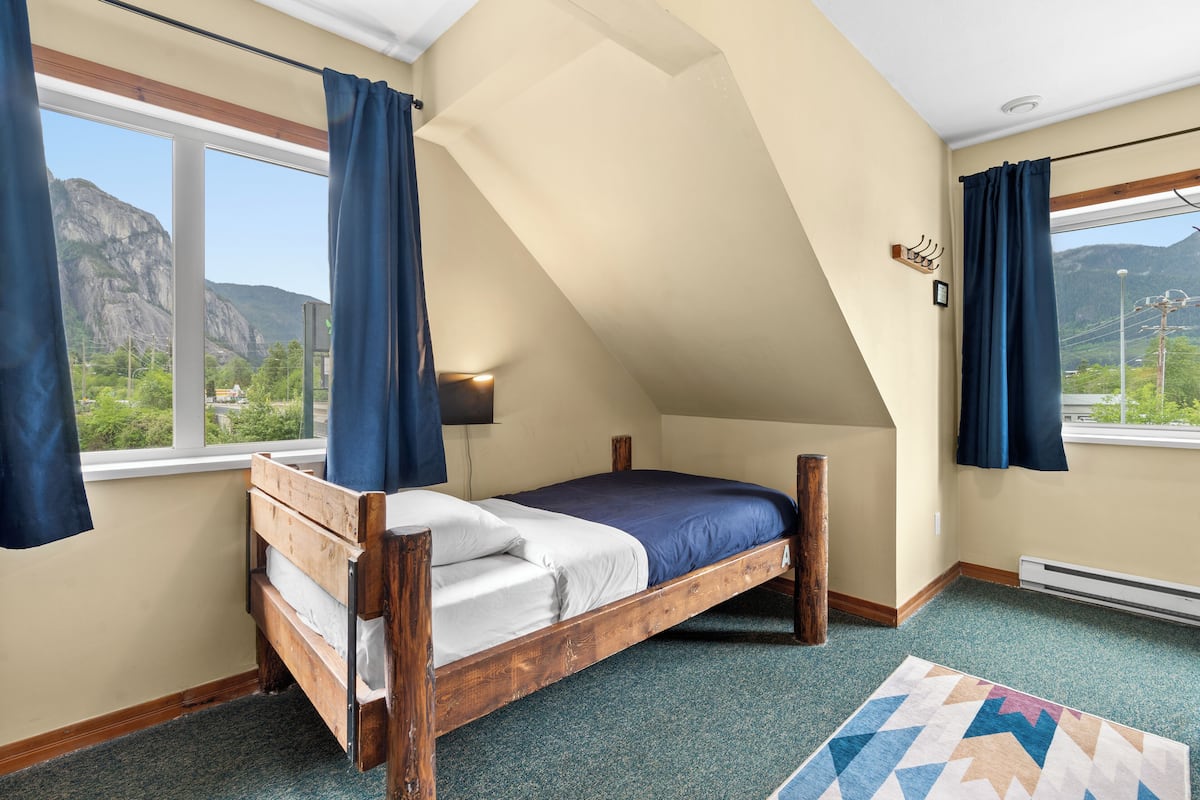 A bedroom with a wooden bed, a view of mountains, and a window with curtains.