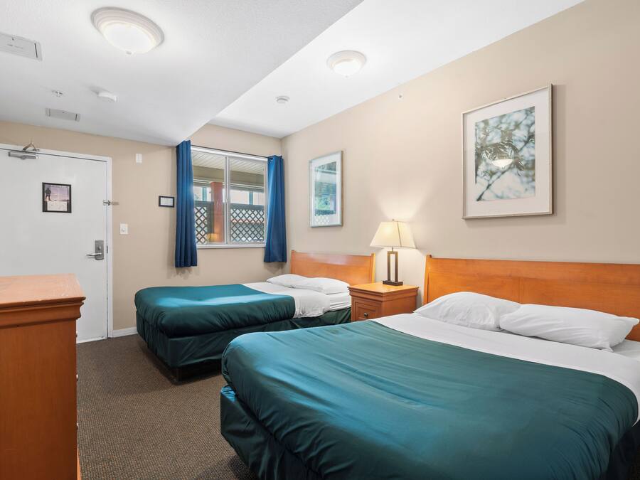 A hotel room with two beds, a desk, a lamp, and a door.