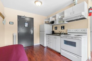 A compact kitchen with white appliances, a microwave, and a stove. There is a door with a lock and a small window.