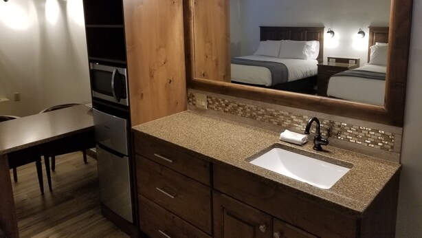 A bathroom with a granite countertop, a sink, a mirror, and a wooden vanity. - Lamplighter Lodge (Panguitch)