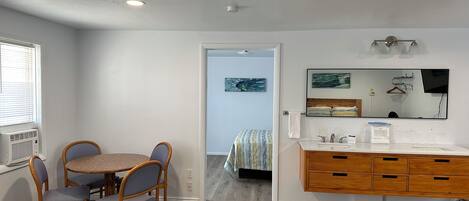 A compact room with a dining table and chairs, a wooden dresser, a mirror, and a television.