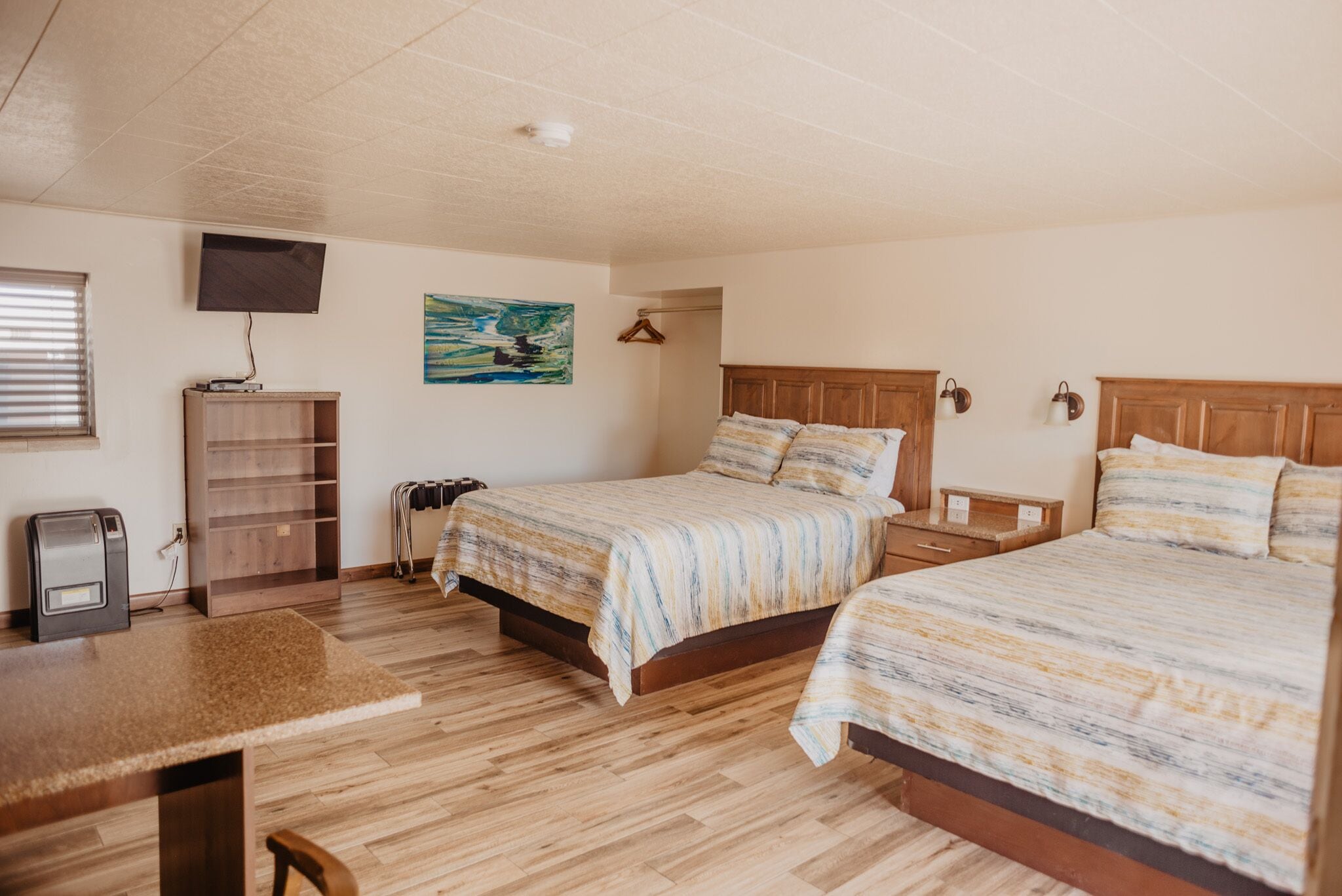 A bedroom with two beds, a desk, a TV, and a painting on the wall.