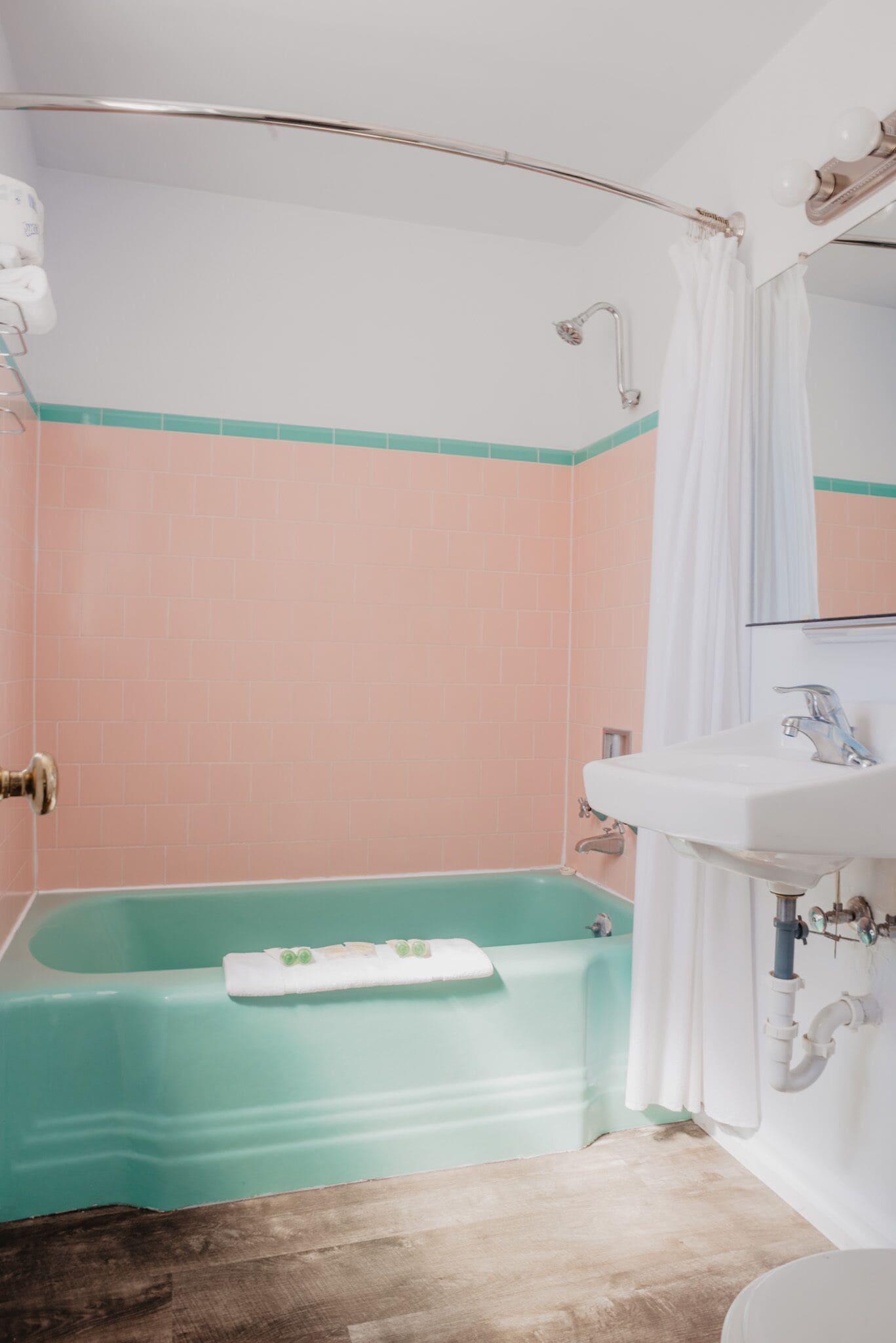 A bathroom with a teal bathtub, a white sink, and a shower with a curved showerhead.