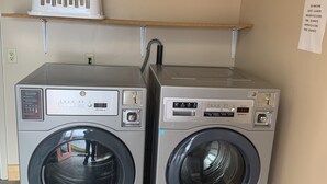 Two front-loading washing machines in a laundry room with a shelf above them holding a white laundry basket. - Lamplighter Lodge (Panguitch)