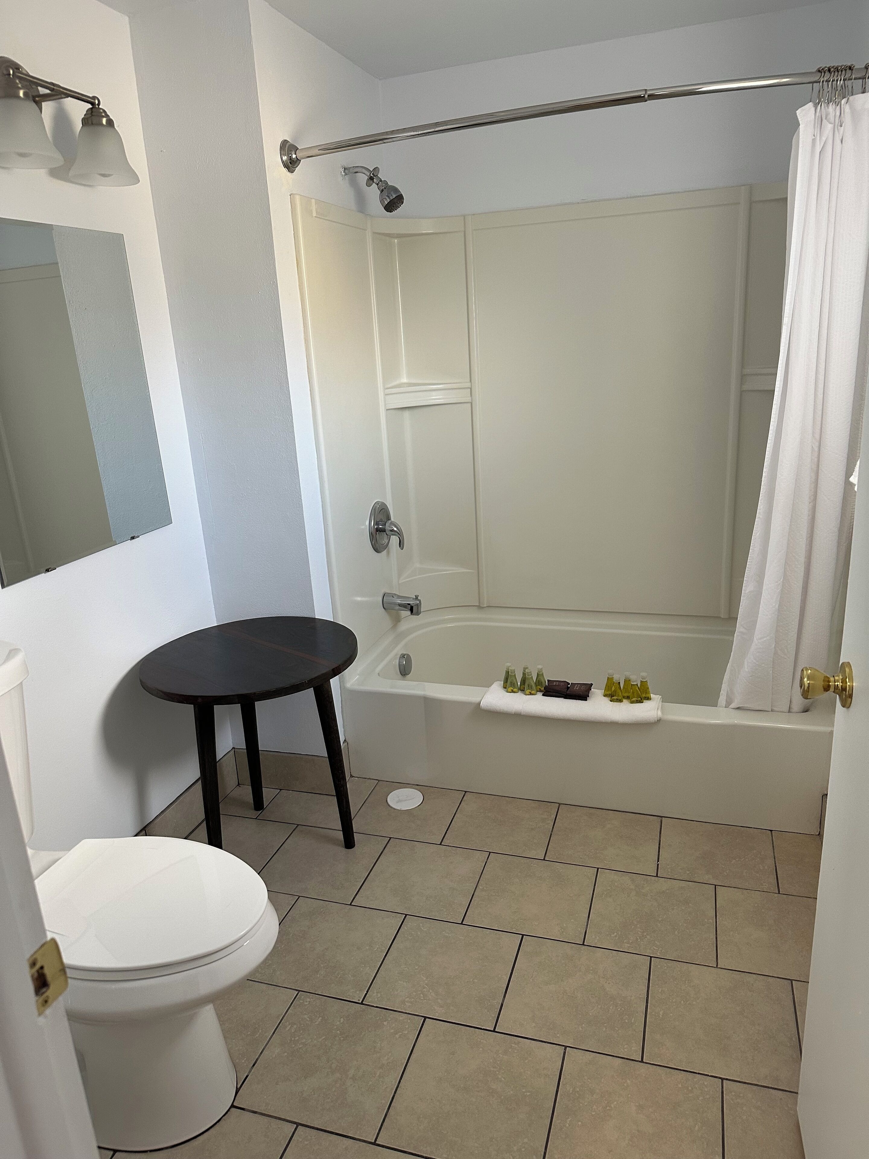 A bathroom with a toilet, a bathtub with a shower curtain, and a small table.